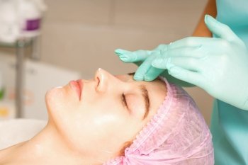 Cosmetologist with gloved hands applies a moisturizing mask with peeling cream on the female face. Facial cosmetology treatment. Procedures for facial care. Cosmetologist with gloved hands applies a moisturizing mask with peeling cream on the female face. Facial cosmetology treatment. Procedures for facial care.