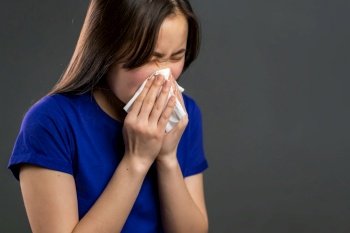 Young asian girl sneezes into tissue. Isolated woman on grey studio background is sick, has a cold or allergic reaction. Coronavirus, epidemic 2020, illness concept.. Young asian girl sneezes into tissue. Isolated woman on grey studio background is sick, has a cold or allergic reaction. Coronavirus, epidemic 2020, illness concept