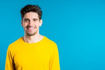 Handsome european man with trendy hairdo in yellow wear on blue studio background. Copy space. Cheerful guy smiling and looking to camera. Handsome european man with trendy hairdo in yellow wear on blue studio background. Copy space. Cheerful guy smiling and looking to camera.