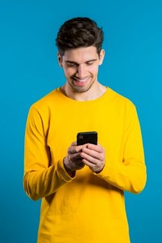 Man sms texting using app on smartphone. Handsome young guy surfing internet with mobile phone. Blue studio background.. Man sms texting using app on smartphone. Handsome young guy surfing internet with mobile phone. Blue studio background