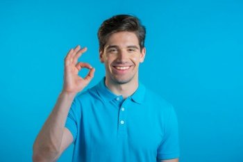 Man showing thumb up sign over blue background. Positive young guy smiles to camera. Winner. Success. Body language. Man showing thumb up sign over blue background. Positive young guy smiles to camera. Winner. Success. Body language.