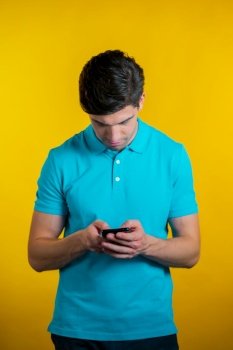 Young man smiling and using mobile phone over yellow background. Handsome european guy holding and texting with smart phone. Boy with technology. Young man smiling and using mobile phone over yellow background. Handsome european guy holding and texting with smart phone. Boy with technology.