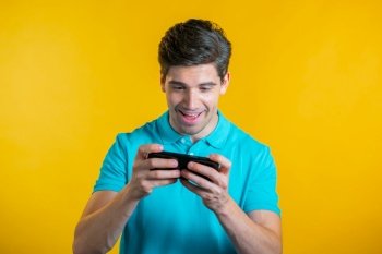 Handsome man playing game on smartphone on yellow studio wall. Using modern technology - apps, social networks. Handsome man playing game on smartphone on yellow studio wall. Using modern technology - apps, social networks.