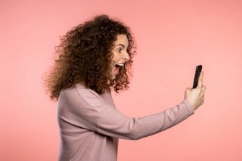 Angry curly woman screaming down, swears with somebody. Using mobile phone. Stressed and depressed girl on pink background. Angry curly woman screaming down, swears with somebody. Using mobile phone. Stressed and depressed girl on pink background.
