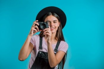 Young pretty woman in overall takes pictures with DSLR camera over blue background in studio. Girl smiling and having fun as photographer. High quality photo. Young pretty woman in overall takes pictures with DSLR camera over blue background in studio. Girl smiling and having fun as photographer.
