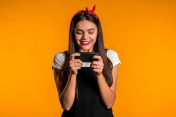 Girl with long hair using smartphone, surfing internet or playing game on studio background. Modern technology - apps, social networks.. Girl with long hair using smartphone, surfing internet or playing game on studio background. Modern technology - apps, social networks