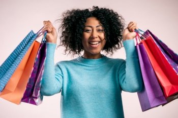 Happy african woman with colorful paper bags after shopping on beige studio background. Concept of seasonal sale, purchases, spending money on gifts. High quality photo. Happy african woman with colorful paper bags after shopping on beige studio background. Concept of seasonal sale, purchases, spending money on gifts