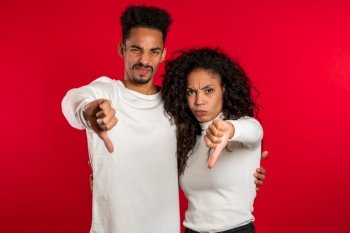 Young african couple standing on red studio background expressing discontent and showing thumb down gesture at camera. Portrait of man and woman with sign of dislike. Young african couple standing on red studio background expressing discontent and showing thumb down gesture at camera. Portrait of man and woman with sign of dislike.