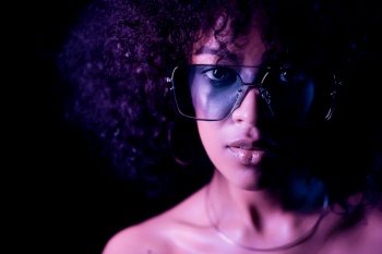 Portrait of young alluring mixed race girl in neon light. Fashion, glamour, model concept. Seductive woman with make-up and transparent glasses posing in dark room at night. Portrait of young alluring mixed race girl in neon light. Fashion, glamour, model concept. Seductive woman with make-up and transparent glasses posing in dark room at night.