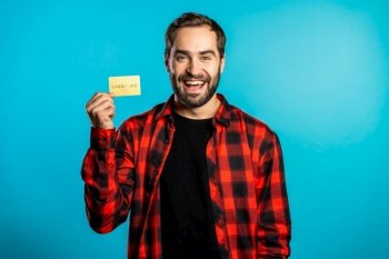 Successful man in plaid shirt showing unlimited gold credit card on blue studio background. Student, money concept.. Successful man in plaid shirt showing unlimited gold credit card on blue studio background. Student, money concept