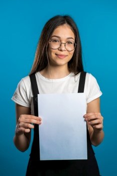 Pretty asian girl holding white a4 paper poster. Copy space. Smiling trendy woman with long hair on studio background. Pretty asian girl holding white a4 paper poster. Copy space. Smiling trendy woman with long hair on studio background.