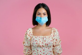 Young pretty girl in face medical mask during coronavirus pandemic. Portrait of girl in floral dress on pink background. Protection with respirator against COVID-19 outbreak.. Young pretty girl in face medical mask during coronavirus pandemic. Portrait of girl in floral dress on pink background. Protection with respirator against COVID-19 outbreak