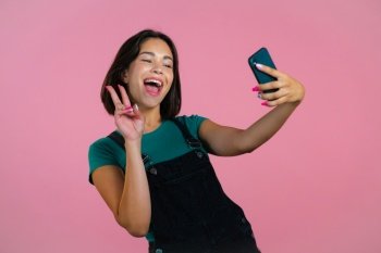Smiling happy woman making selfie on smartphone over pink background. Technology, mobile device, social networks concept.. Smiling happy woman making selfie on smartphone over pink background. Technology, mobile device, social networks concept