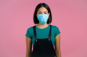 Young pretty girl in face medical mask during coronavirus pandemic. Portrait on pink background. Protection with respirator against COVID-19 outbreak.. Young pretty girl in face medical mask during coronavirus pandemic. Portrait on pink background. Protection with respirator against COVID-19 outbreak