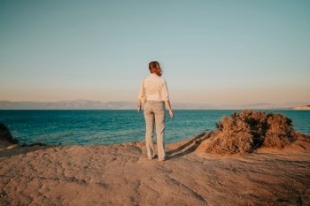 Unrecognizable woman standing near cliff over Mediterranean Ionian sea. Lady watching beautiful blue water surface alone, nature background. Windy weather, golden hour. High quality photo. Unrecognizable woman standing near cliff over Mediterranean Ionian sea. Lady watching beautiful blue water surface alone, nature background. Windy weather, golden hour.