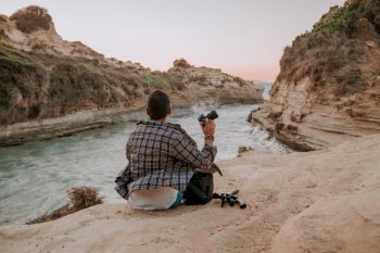 Stranger man hipster photographer sitting on seashore near love channel - Canal D’Amour on Corfu island. Nature videography. High quality photo. Stranger man hipster photographer sitting on seashore near love channel - Canal D’Amour on Corfu island. Nature, sea videography.