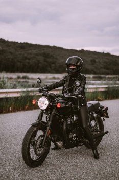 Stylish motorcyclist woman in helmet and leather jacket sitting on vintage motorcycle. Female driver outdoors on nature background. Trip, cafe racers, speed, freedom concept. High quality photo. Stylish motorcyclist woman in helmet and leather jacket sitting on vintage motorcycle. Female driver outdoors on nature background. Trip, cafe racers, speed, freedom concept.