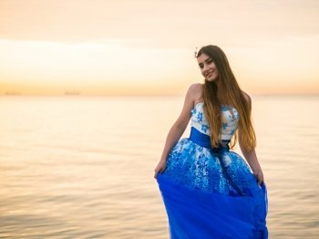 Young beautiful woman dances in blue princess evening or ball dress on pier close to sea. High quality photo. Young beautiful woman dances in blue princess evening or ball dress on pier close to sea.