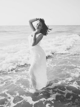 Gypsy young brunette girl in white maxi long dress standing on the waves in sea or ocean. Windy beach. Bohemian lifestyle. Portrait of happy sexy woman.. Gypsy young brunette girl in white maxi long dress standing on the waves in sea or ocean. Windy beach. Bohemian lifestyle. Black and white portrait of happy sexy woman.