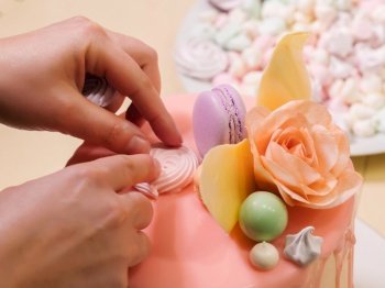 Unrecognisable woman decorating mousse glaze cake, hands detail, focus on the cake. DIY, sequence, step by step, part of series.. Unrecognisable woman decorating mousse glaze cake with rose, macarons, hands detail, focus on the cake. DIY, sequence, step by step, part of series.