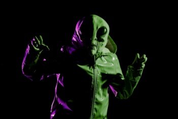 Futuristic alien showing frightening gesture, trying to scare. Creepy mask of humanoid on neon extraterrestrial planet masquerading as human person in smooth raincoat. UFO, fiction concept. photo. Futuristic alien showing frightening gesture, trying to scare. mask of humanoid