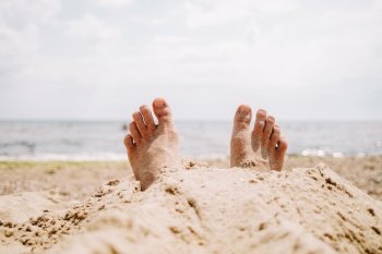 Male feet in sand on beach. Sunbathing, summer vacation, tan concept. Happy tourist rests near sea or ocean. High quality photo. Male feet in sand on beach. Sunbathing, summer vacation, tan concept