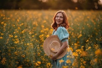 Portrait of attractive woman posing in blooming canola flowers field. Elegant girl in retro dress with straw hat, countryside nature place. Rapeseed meadow, vintage outfit, spring season. Happy woman in blooming canola flowers field. Lady in retro dress, spring season