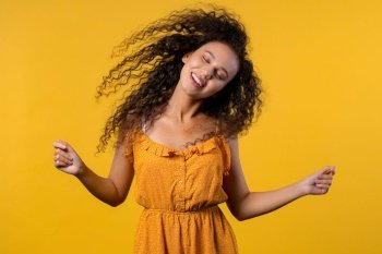 Woman dancing with big afro curly hair on yellow backdrop, hairstyle flying air. High quality photo. Woman dancing with big afro curly hair on yellow backdrop, hairstyle flying air