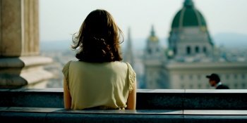 Vertical shot of auburn brown haired 30 years old woman looks at crowded city at rooftop of a temple, Vienna Austria