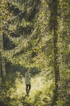 Young woman walking along sunny fir wood scenic photography. Picture of person with woodland on background. High quality wallpaper. Photo concept for ads, travel blog, magazine, article. Young woman walking along sunny fir wood scenic photography