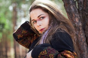 Close up young woman with shaman makeup leaning on tree portrait picture. Closeup side view photography with forest on background. High quality photo for ads, travel blog, magazine, article. Close up young woman with shaman makeup leaning on tree portrait picture