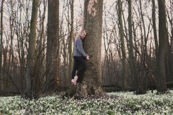 Blonde woman hugging large tree trunk scenic photography. Picture of person with deep forest on background. High quality wallpaper. Photo concept for ads, travel blog, magazine, article. Blonde woman hugging large tree trunk scenic photography