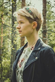 Close up young model in stylish clothes in park portrait picture. Closeup side view photography with spring forest on background. High quality photo for ads, travel blog, magazine, article. Close up young model in stylish clothes in park portrait picture