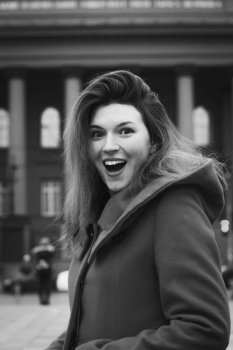 Close up happy emotional woman on street monochrome portrait picture. Closeup side view photography with city building on background. High quality photo for ads, travel blog, magazine, article. Close up happy emotional woman on street monochrome portrait picture