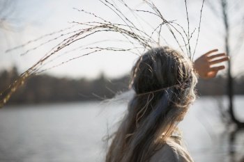 Close up looking at lake woman with long willow twigs crown portrait picture. Closeup rear view photography with blurred background. High quality photo for ads, travel blog, magazine, article. Close up looking at lake woman with long willow twigs crown portrait picture