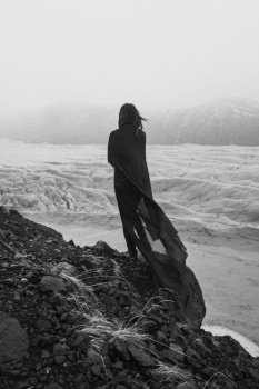 Lady wrapped with gentle fabric on cliff monochrome scenic photography. Picture of person with old glacier on background. High quality wallpaper. Photo concept for ads, travel blog, magazine, article. Lady wrapped with gentle fabric on cliff monochrome scenic photography