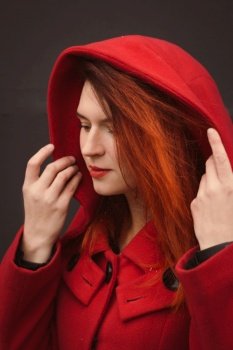 Close up attractive lady adjusting large coat hood portrait picture. Closeup side view photography with dark grey background. High quality photo for ads, travel blog, magazine, article. Close up attractive lady adjusting large coat hood portrait picture