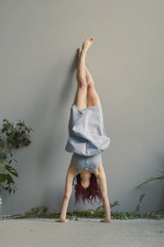 Handstand against wall funny pose scenic photography. Picture of woman in linen dress with house plants on background. High quality wallpaper. Photo concept for ads, travel blog, magazine, article. Handstand against wall funny pose scenic photography
