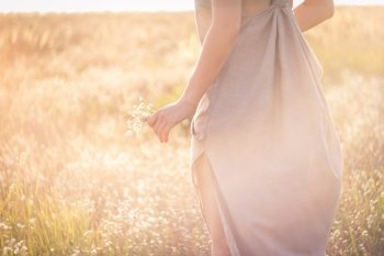 Close up woman with flowers surrounded by sunlight glare concept photo. Side view photography with blooming meadow on background. High quality picture for wallpaper, travel blog, magazine, article. Close up woman with flowers surrounded by sunlight glare concept photo