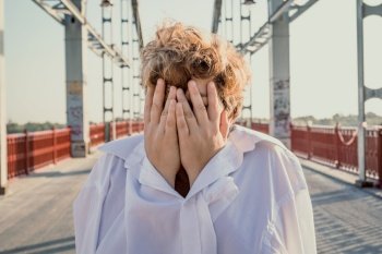 Close up short haired woman covering face with hands portrait picture. Closeup front view photography with blurred bridge background. High quality photo for ads, travel blog, magazine, article. Close up short haired woman covering face with hands portrait picture