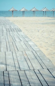 Wooden walkway to water seascape photo. Sand beach. Beautiful scenery photography with straw umbrellas on background. Idyllic scene. High quality picture for wallpaper, travel blog, magazine, article. Wooden walkway to water seascape photo