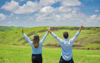 Back view of Happy couple in the field raising hands to the sky, Concept of a happy and free couple in the field, Back view of couple on the hill with hands raised to the sky