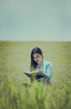 A person sitting on the grass reading a book, Attractive people sitting on the grass reading a book, A girl reading a book in the field