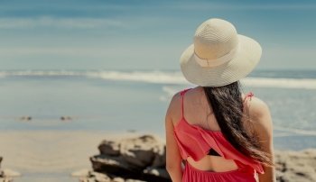 Back view of girl with hat looking at the sea, Young woman in hat looking at the sea on vacation, Concept of girl enjoying vacation on the beach, Rear view of a girl looking at the sea