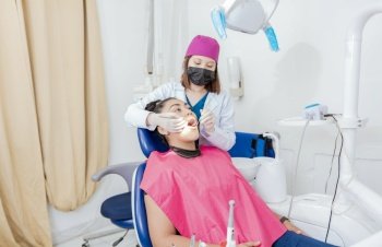 Female dentist with probe and dental mirror examining mouth to lying patient. Health and dental care concept, Dentist doctor examining mouth to female patient lying on chair