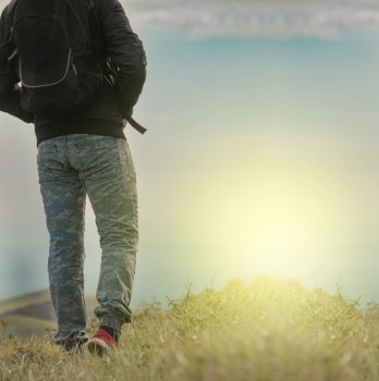 Backpacker man walking in field back view, close up of man from behind in field, low angle of backpacking man with copy space
