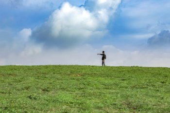 A backpacker on a hill with blue sky and copy space, man backpacking on a green hill with copy space, concept of successful man spreading his hands