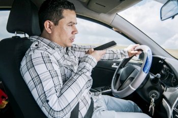 Man in his car sending voice notes with his cell phone, Side view of a young man sitting inside the car talking on the phone while driving, Young man sitting in the car talking on the phone while driving