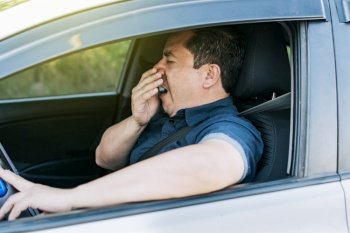 Tired driver yawning, concept of man yawning while driving. A sleepy driver at the wheel, a tired person while driving