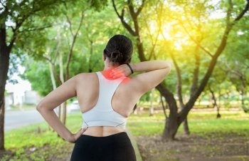 Running woman with shoulder muscle pain in a park. Shoulder pain concept of a runner athlete. Athlete girl in pain rubbing her shoulder outdoors. Back view of sporty woman with shoulder pain